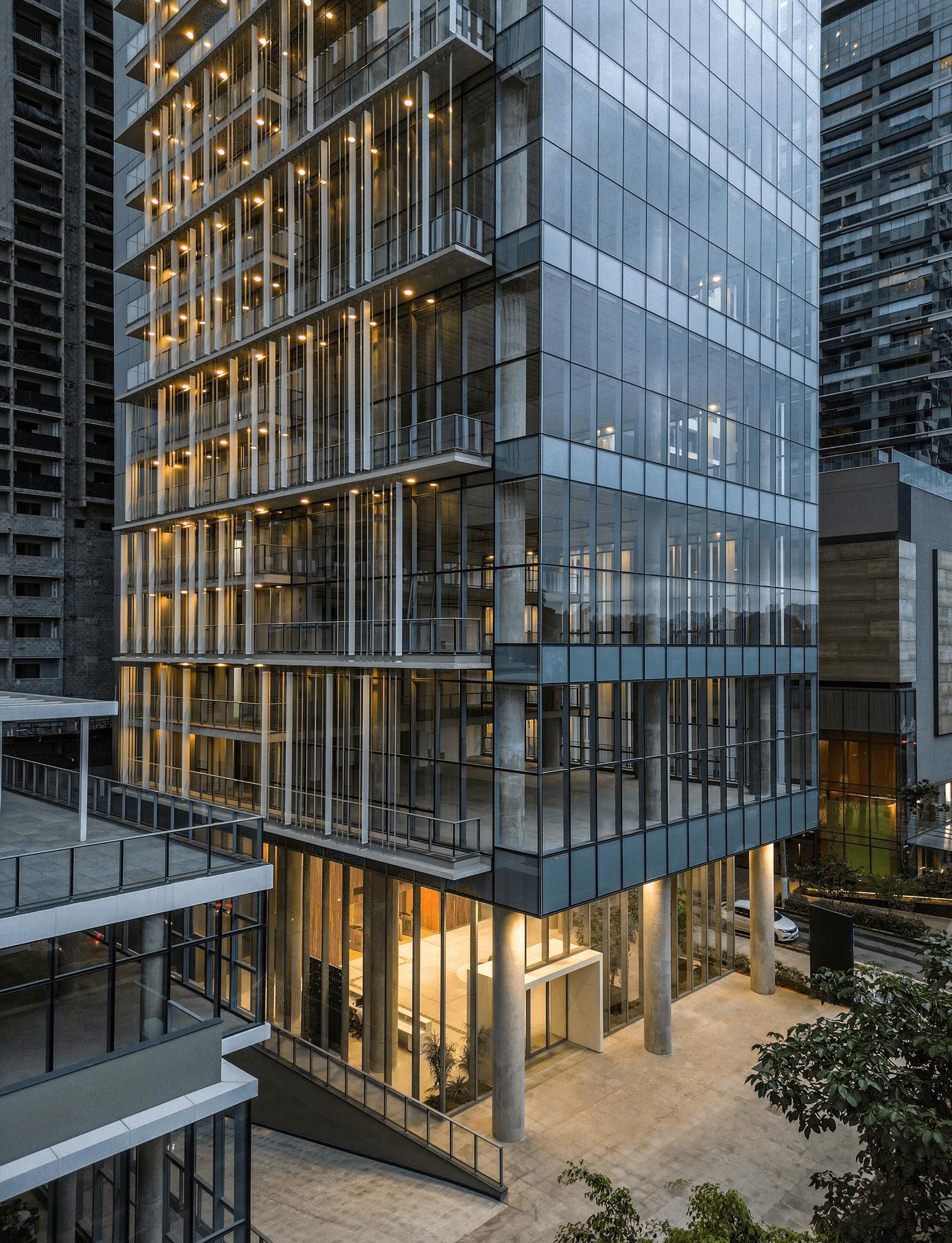 Fachada de vidro e concreto de edifício corporativo contemporâneo, com aletas verticais iluminadas ao entardecer.